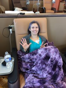 Jelena sitting in a chemo chair with a purple blanket in her lap holding up 7 fingers